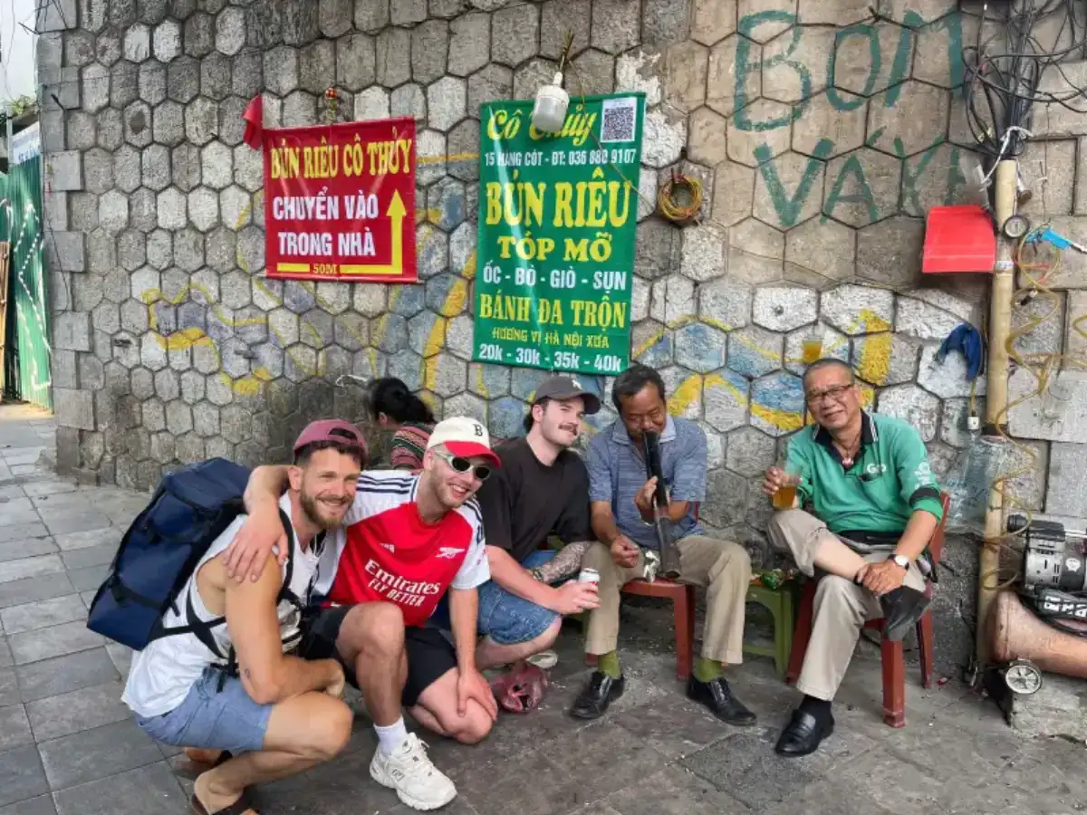 Travelers on a private walking tour in Hanoi sitting with locals and enjoying street food in the Old Quarter
